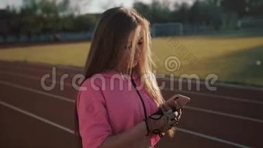 跑步者在红色跑步轨道上听智能手机音乐应用程序。 带着耳机和智能手机的女运动员